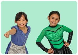 Two young girls in colorful costumes pose and smile against a mint green background one reaching toward the camera and the other in a green sequined outfit