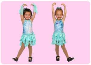 Two young girls in turquoise dance costumes pose with arms raised overhead against a pink background